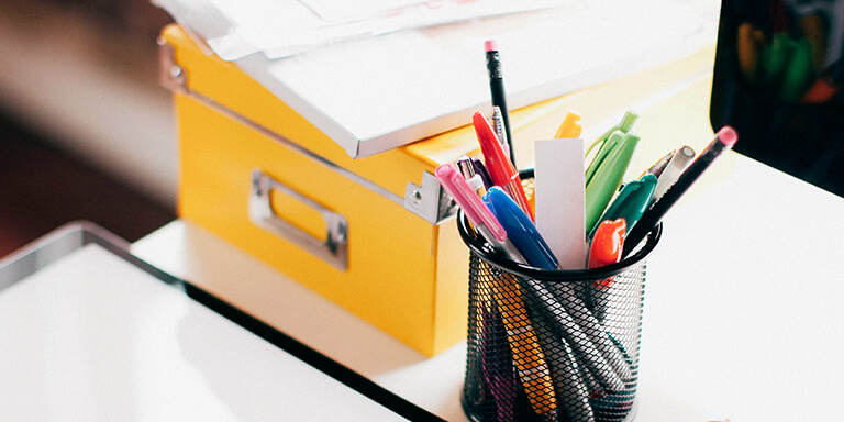 A cup of colorful pens and a yellow box on a desk 