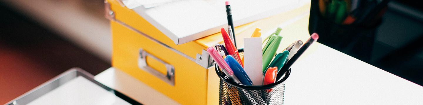 A cup of colorful pens and a yellow box on a desk 