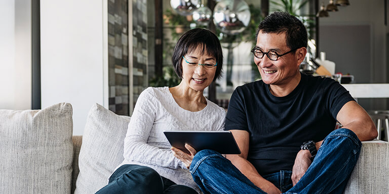 A man and woman looking at a tablet together on the couch