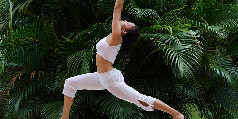 A woman in athletic clothes doing yoga poses in front of a wall of plants