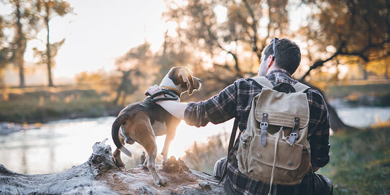 Man and his dog taking a rest from walking, sitting by the river, enjoying the view and sunset