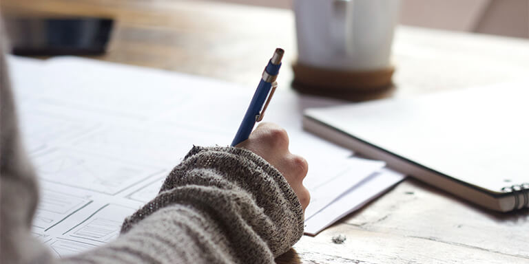Woman taking notes with a pen at a wooden table 