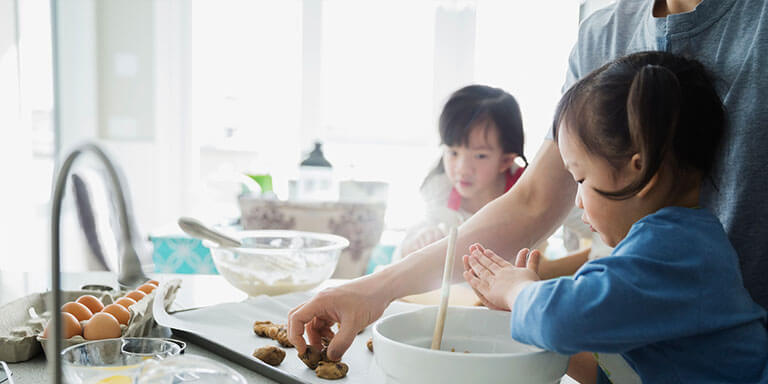 A father and his young daughters washing their hands while baking in their kitchen