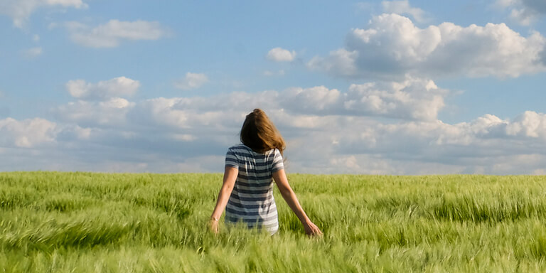 Woman standing with her arms outstretched in a large field of grass with the wind blowing