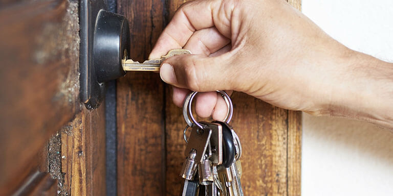 A man inserting a key into the lock of a wooden front door to a house