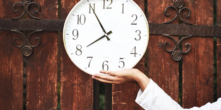 Two people holding up a white clock in front of antique wooden doors