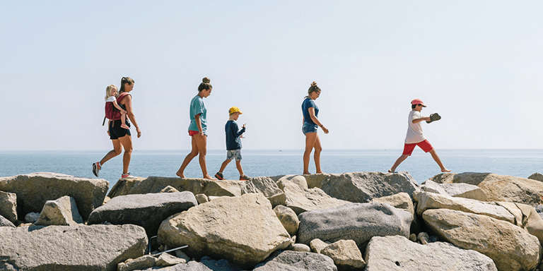 A family of 6 walking along a pile of rocks on the coast near the ocean