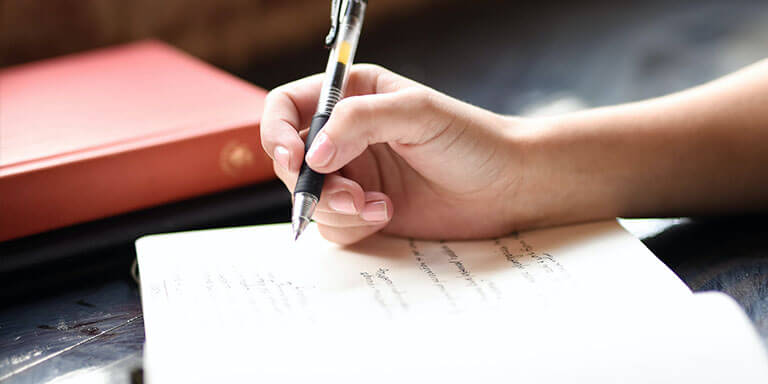 Close up of a woman writing in a journal next to a stack of books