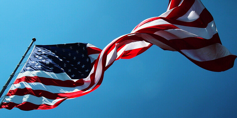 A large American flag blowing in the wind against a clear blue sky