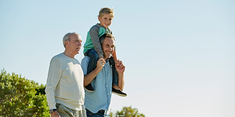 A young boy sitting on his fathers shoulders with his grandfather on a beach