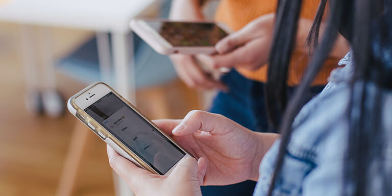 A close up of a woman reading something on her phone while standing next to her friend