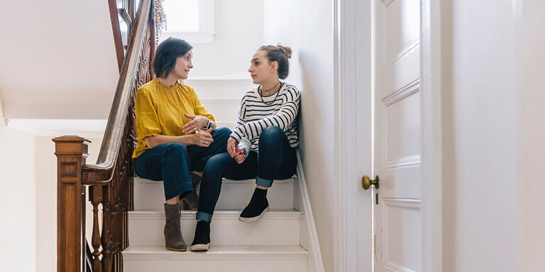 Two women sitting on the stairs facing each other and having a discussion
