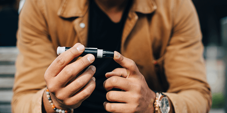 A man in a tan jacket checking his blood sugar levels by pricking his fingertip