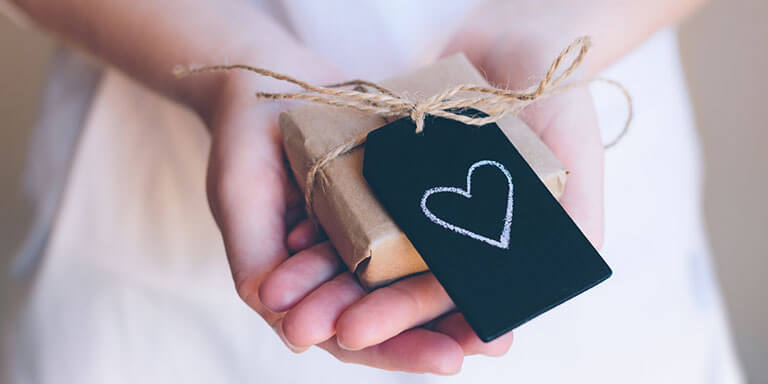 Woman holding a present wrapped in brown paper with a black tag with a white heart on it