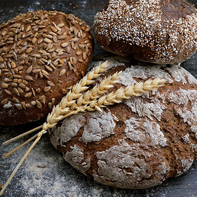 Close up of 3 different kinds of baked breads, with a sprig of wheat laying against them 