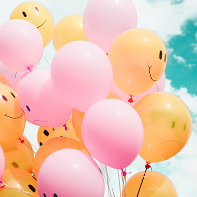 A collection of pink and orange balloons with smiley faces and frowning faces against a blue sky
