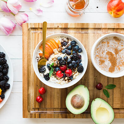 An overhead of a breakfast of oatmeal, coffee, fruit, and avocados laid out on a cutting board 