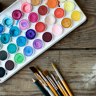 A close-up of a used watercolor palette and an assortment of different sized paintbrushes 