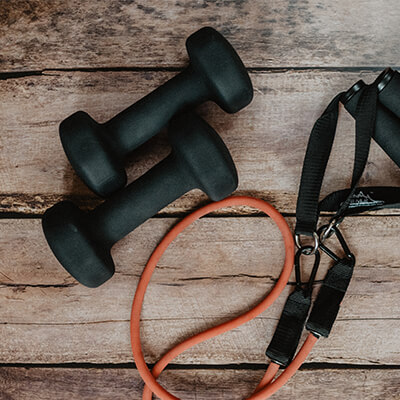 A close-up of two black dumbbells and a rubber resistance band against some hardwood floors 