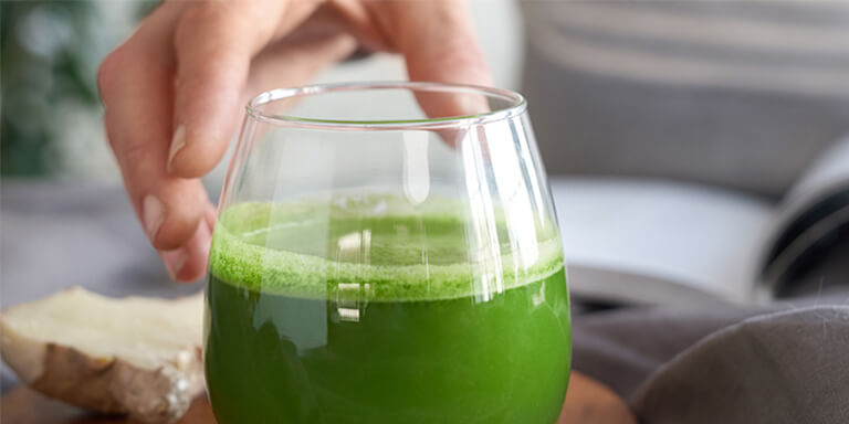 Man reaching for an organic green smoothie on a kitchen counter