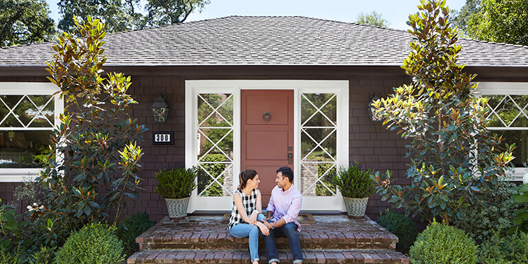 Young couple sitting on the front steps of the home they purchased together