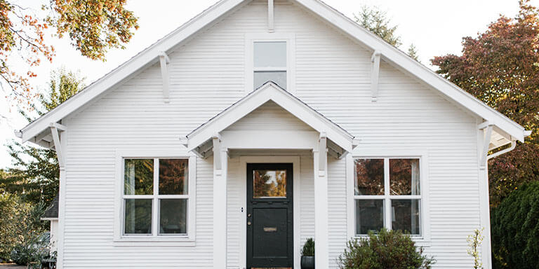 White wooden house with a black painted front door in the fall foliage 