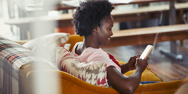 A woman sitting on a plaid couch smiling at her smart phone