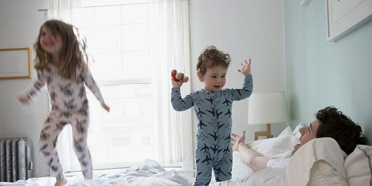 Two young children in pajamas jumping on their parents bed in the early morning