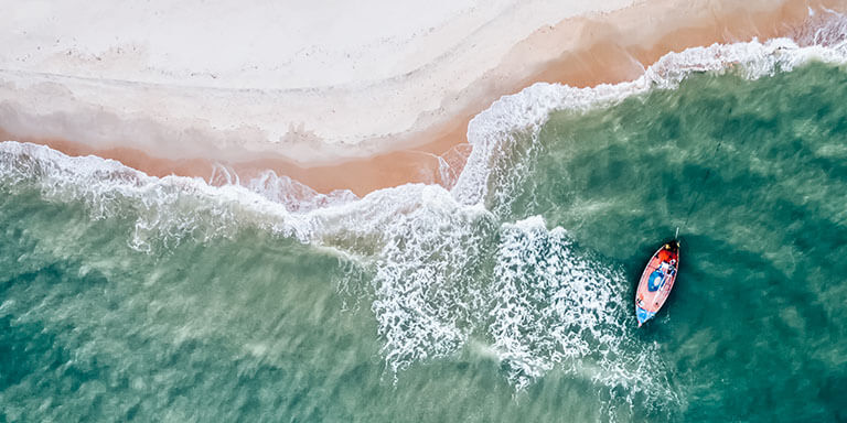 Aerial view of a boat anchored in the ocean on the coast of a pink sand beach