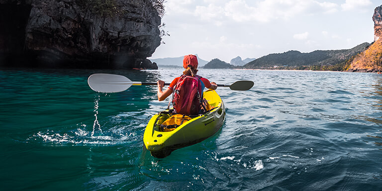 A woman wearing red paddling a yellow kayak in open waters surrounded by islands