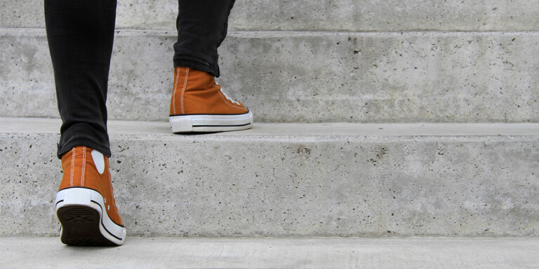 A person in black jeans and tan sneakers walking up concrete steps