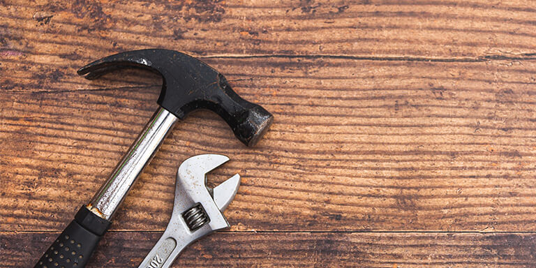 A close-up of a hammer and a wrench against a wooden tabletop 