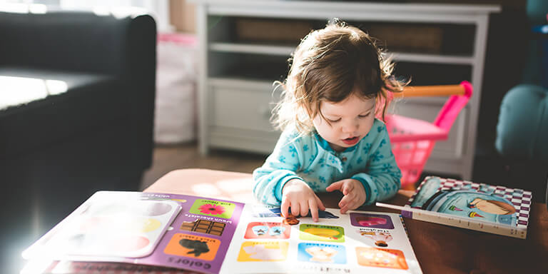 A young girl reading children's books at a coffee table in her living room 