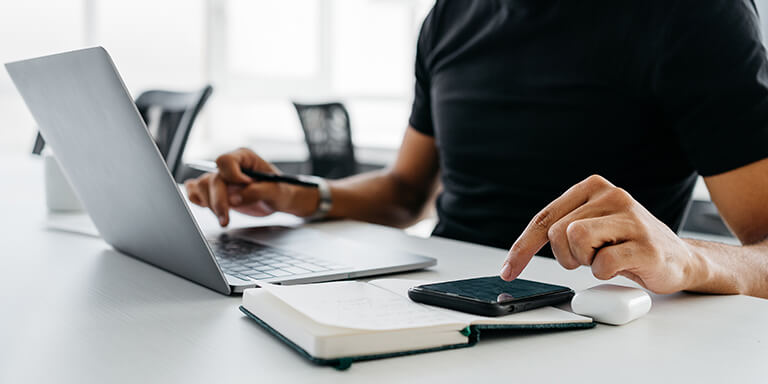 Man looking at something on his smartphone and typing on his laptop computer 