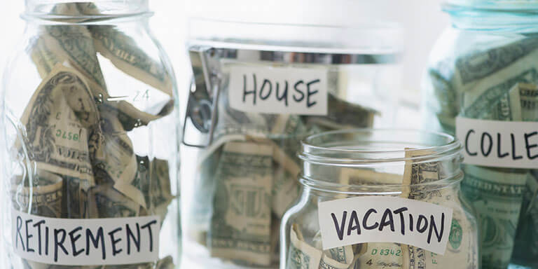 4 Glass jars labeled with "Retirement", and "College", "Vacation",  and filled with dollar bills. 