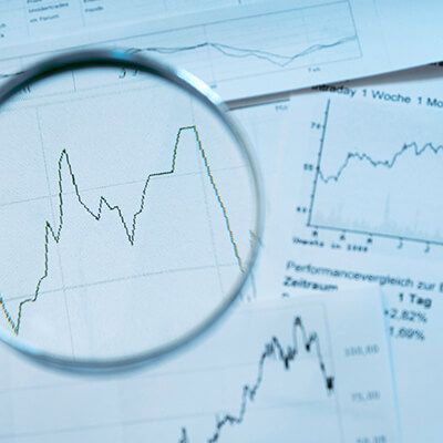 Paper showing stock market numbers and graphs with a magnifying glass on top