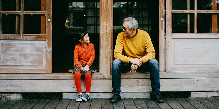 A grandfather and granddaughter sitting together on a porch