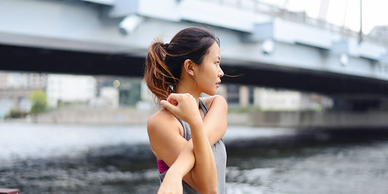 A woman on a running path underneath a bridge stretching 