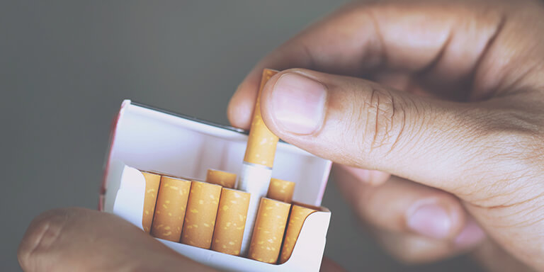 Close up of a man pulling a single cigarette out of a carton