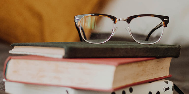 A pair of reading glasses resting on top of a stack of colorful books