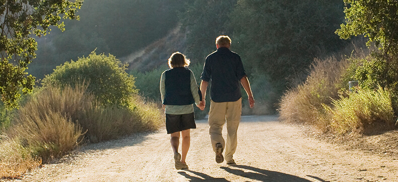 A middle aged couple walking together on an outdoor trail holding hands