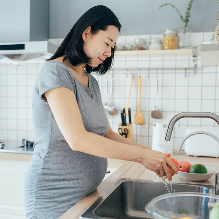 An expecting mother washing fruit at the sink in her kitchen