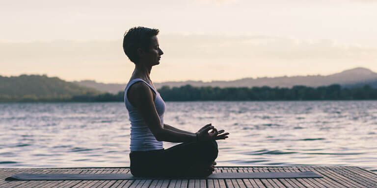 Woman wearing athletic clothes meditating on a dock on a lake at sunrise