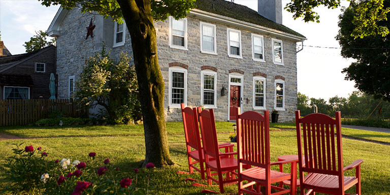 A gray stone house surrounded by trees and red rocking chairs 