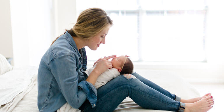 A new mother holding her infant daughter on her knees on her bed 