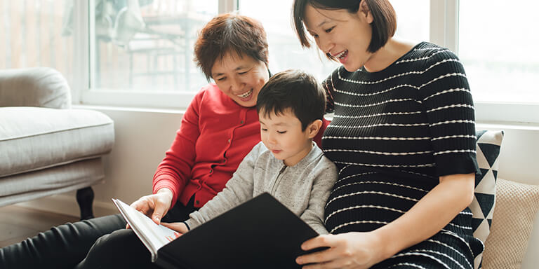 A young boy, his mother and his grandmother reading together on a couch
