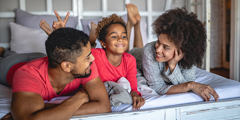 a young boy and his parents laughing on a bed together