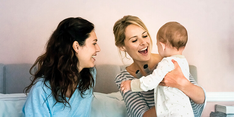 A woman holding her baby while her parter smiles at them