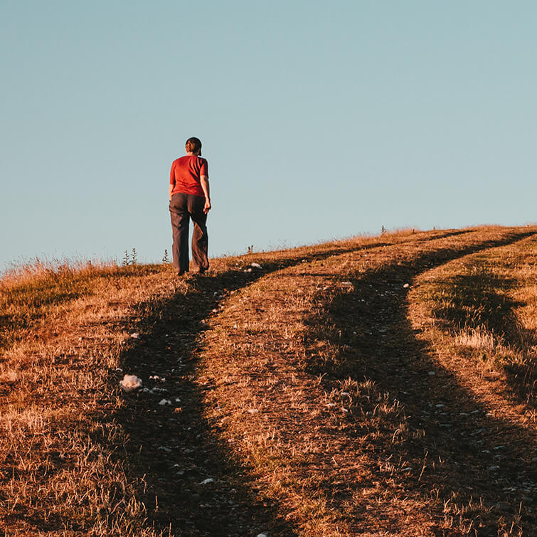 A woman walking up an incline along a dirt road. 