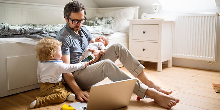 Father with his little son and baby daughter working on his computer from home